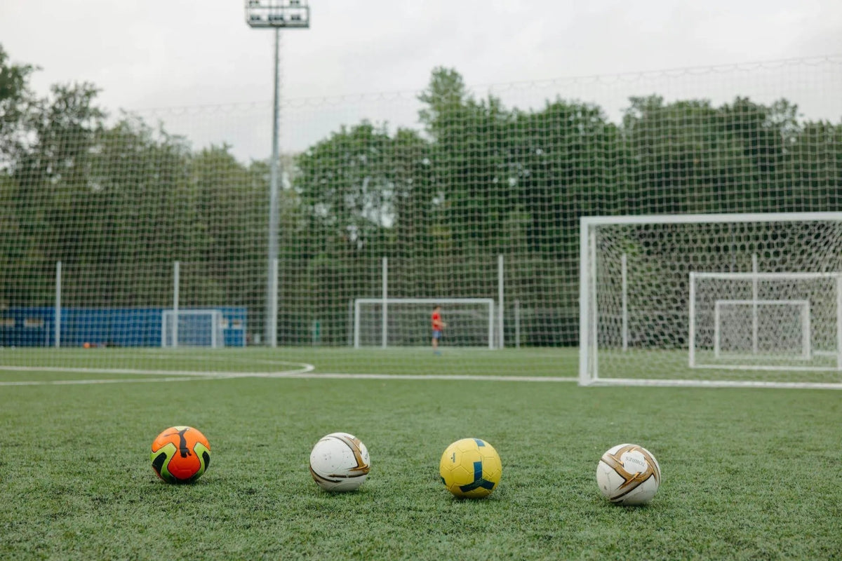 Four different soccer balls next to each other on a soccer pitch