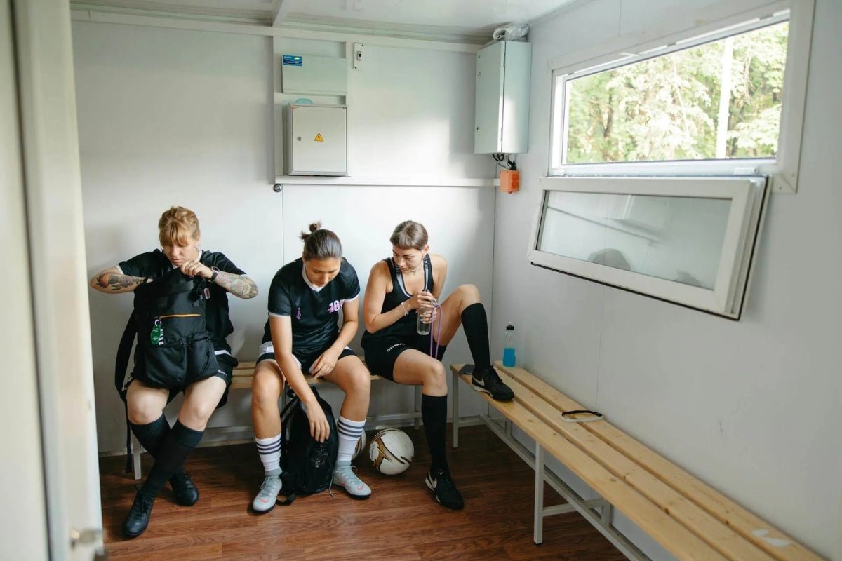 Three female soccer players sitting in locker room bench in their black uniforms