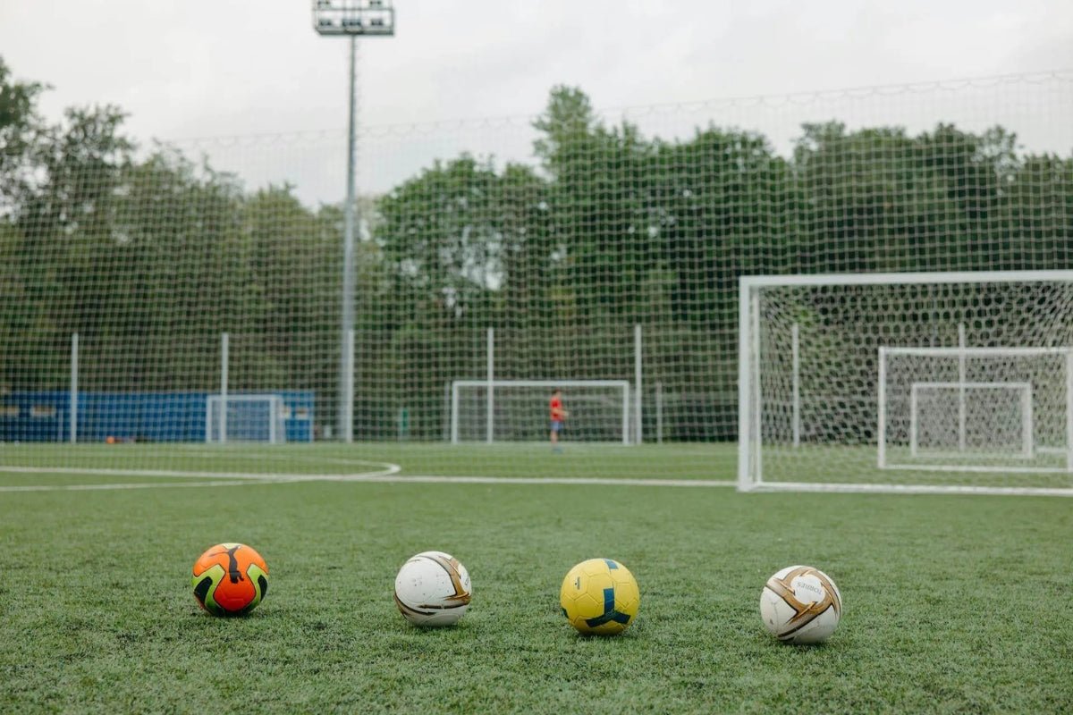 Four different soccer balls next to each other on a soccer pitch
