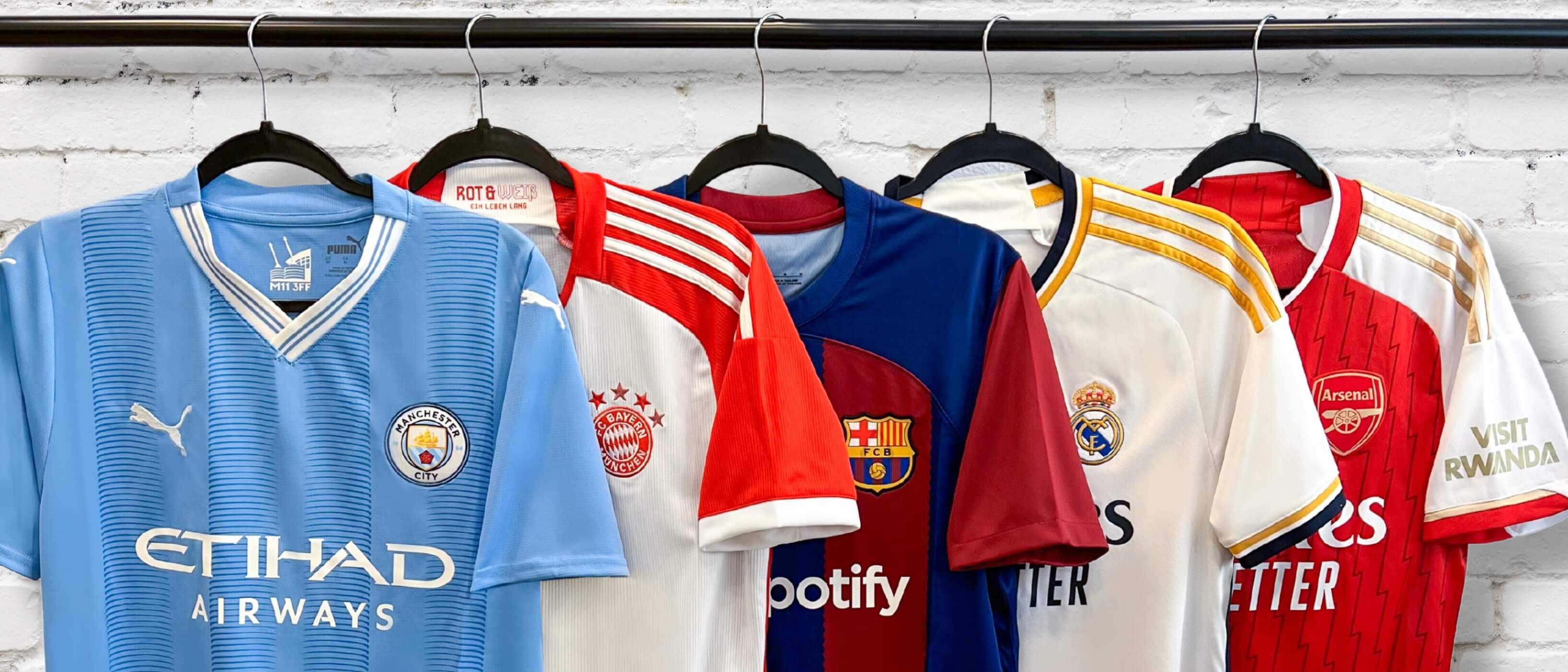 5 different soccer club team jerseys hanging from coat hangers next to each other