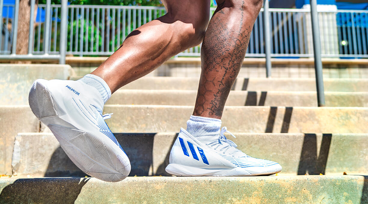 athlete wearing white adidas indoor soccer shoes while going up concrete stairs