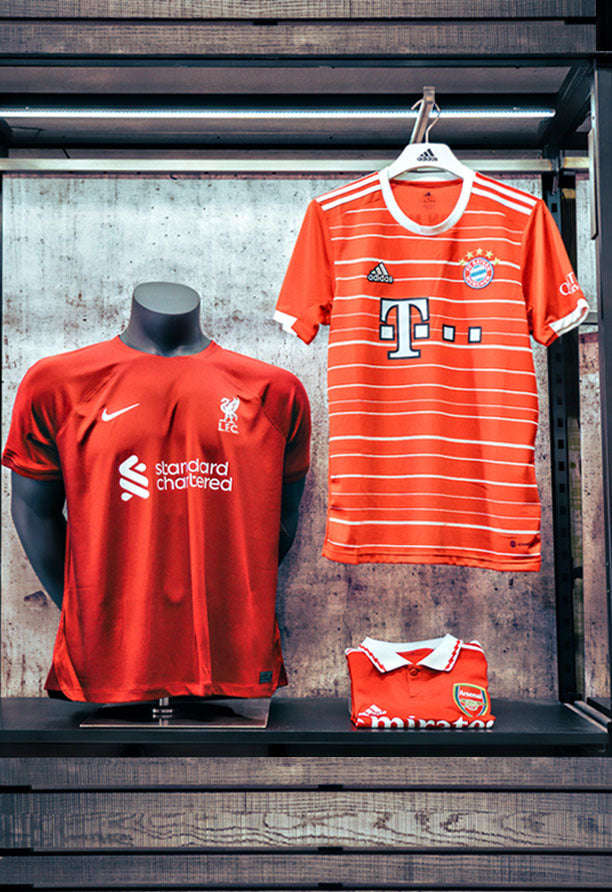 Liverpool jersey by Nike and Bayern Munich jersey by adidas on mannequin and hanger next to each other.
